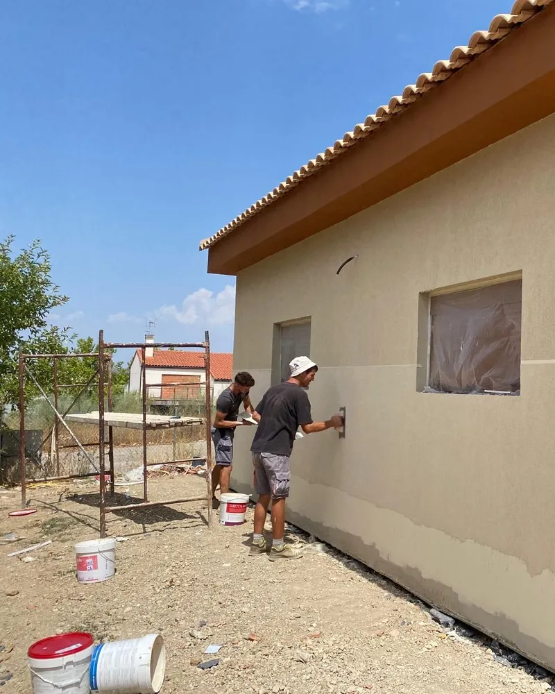 Dos operarios aplicando el acabado del SATE en la fachada de una casa de una planta