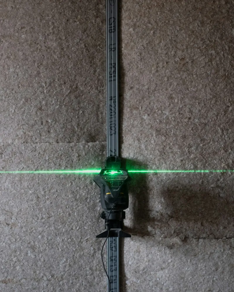 Nivel láser sobre una pared con panel de fibra aislante y perfil metálico