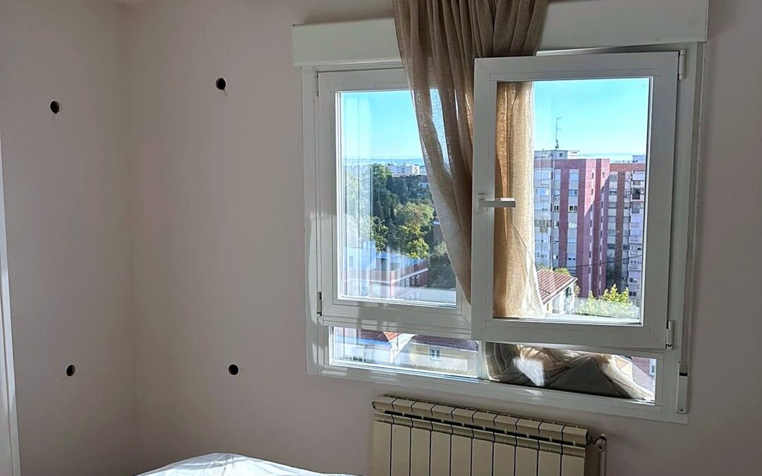 Dormitorio con ventana y radiador y pequeños orificios en la pared para insuflar aislante en la cámara de aire
